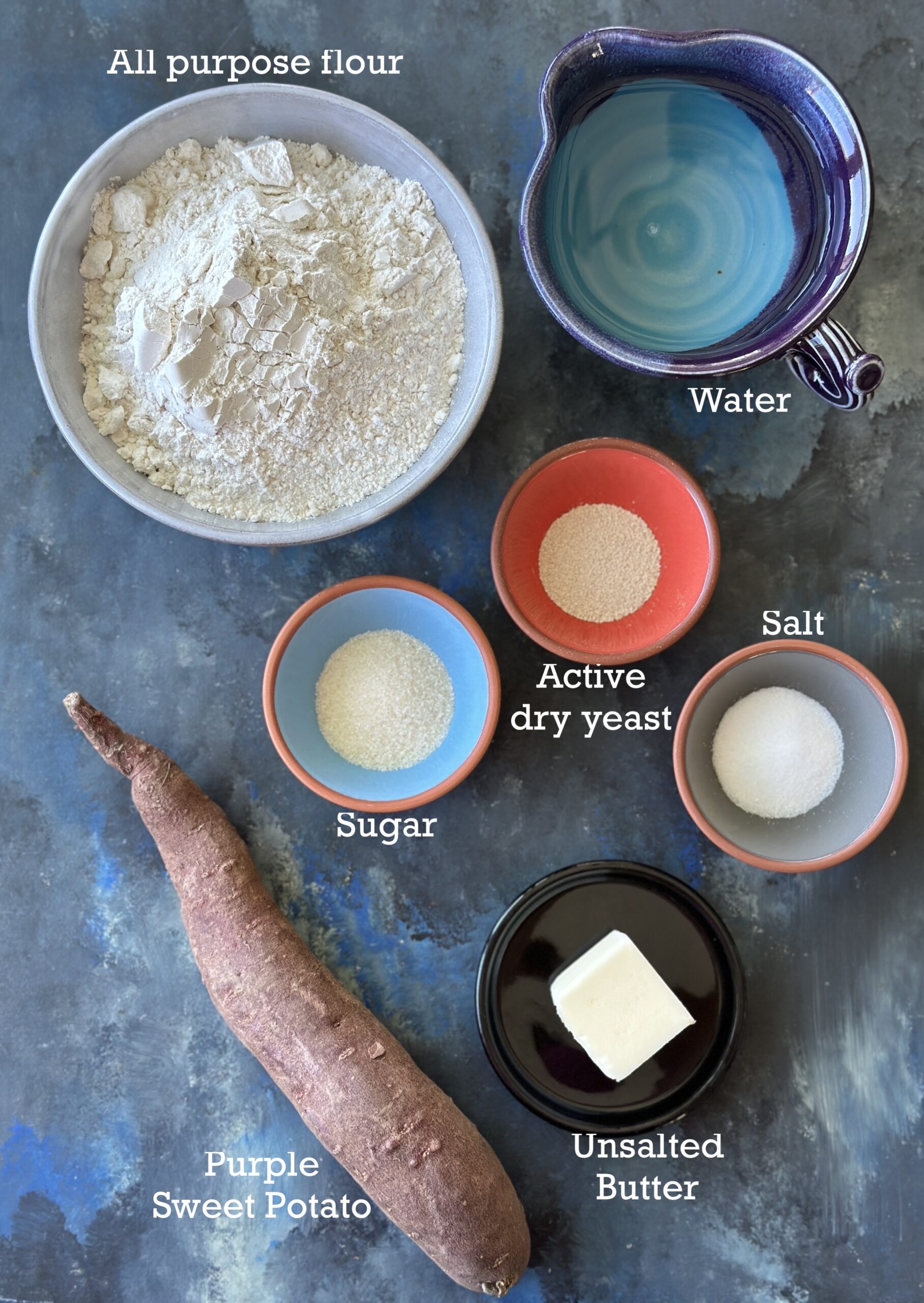 Ingredients for Purple Sweet Potato Bread; flour, yeast, sweet potato among others on a black blue background. 
