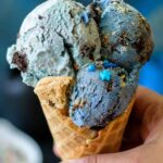 Hand holding a cone with blue colored cookie monster ice cream topped with sprinkles.