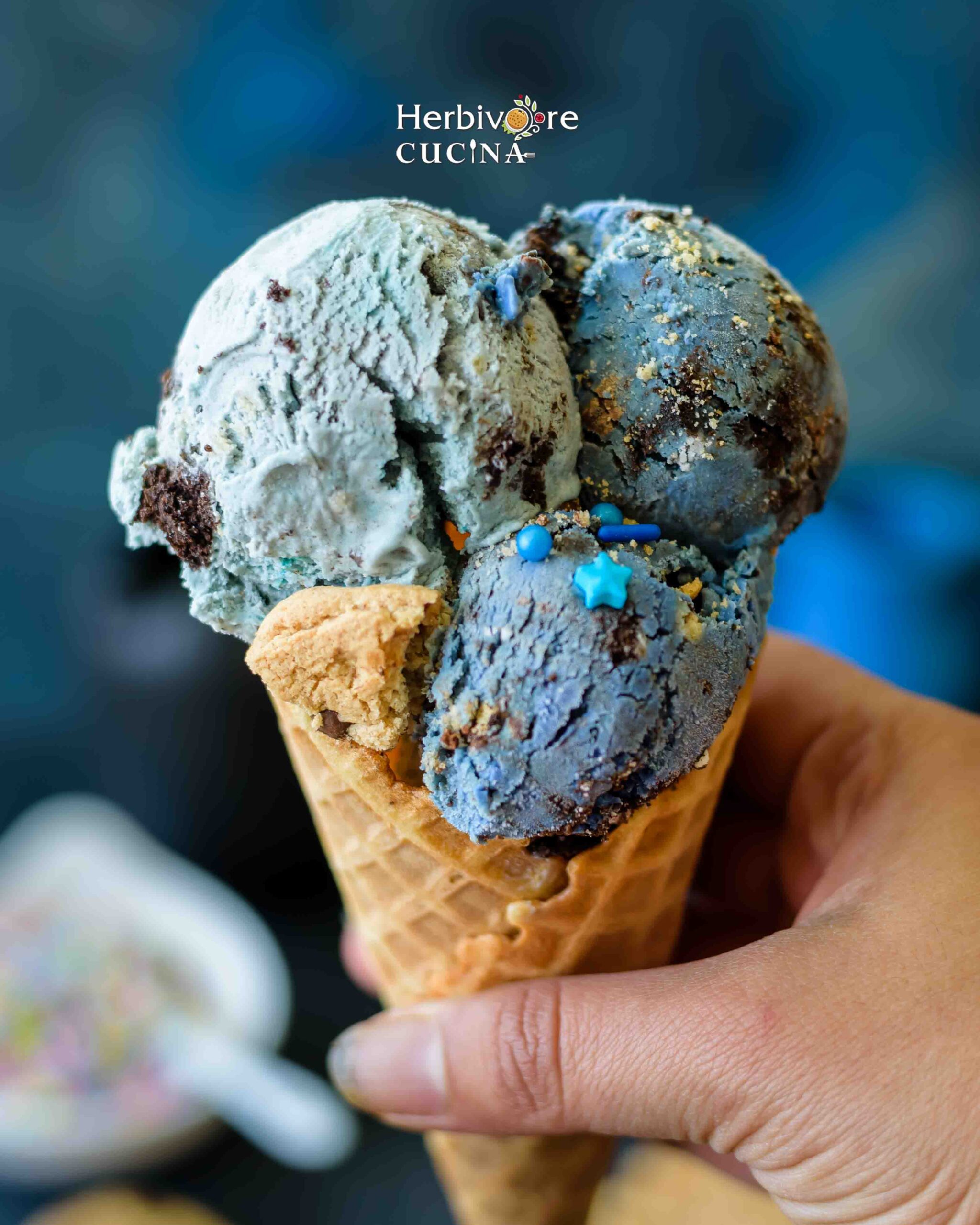  hand holding a cone with blue colored cookie monster ice cream topped with sprinkles. 