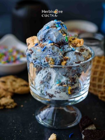 A glass bowl with cookie monster ice cream with cookies and sprinkles.