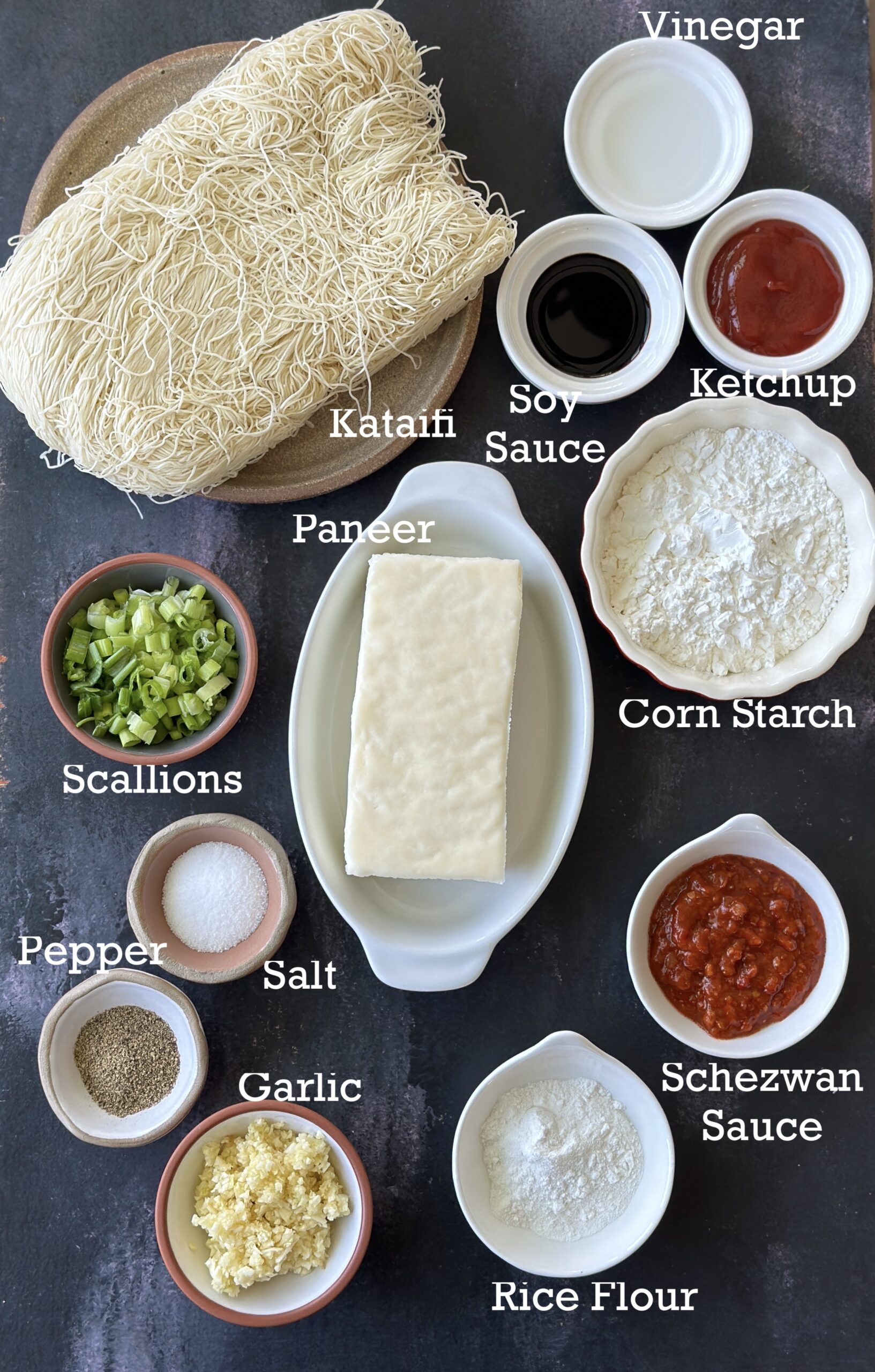 Ingredients for Crispy Thread Paneer; paneer kataifi and other seasonings on a black background. 