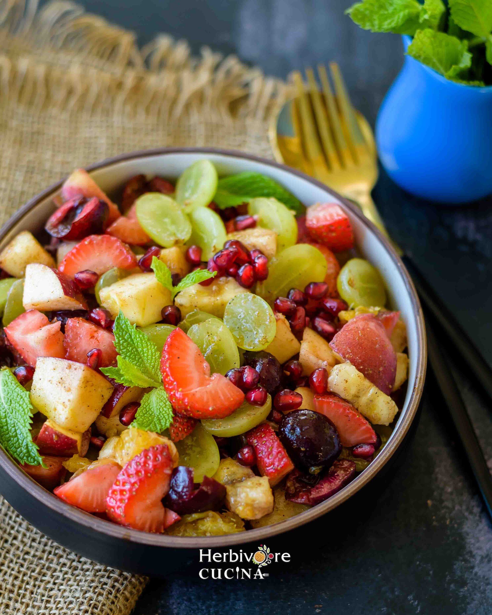 Side view of a black and white bowl filled with fruit chaat and topped with a sprig of mint. 