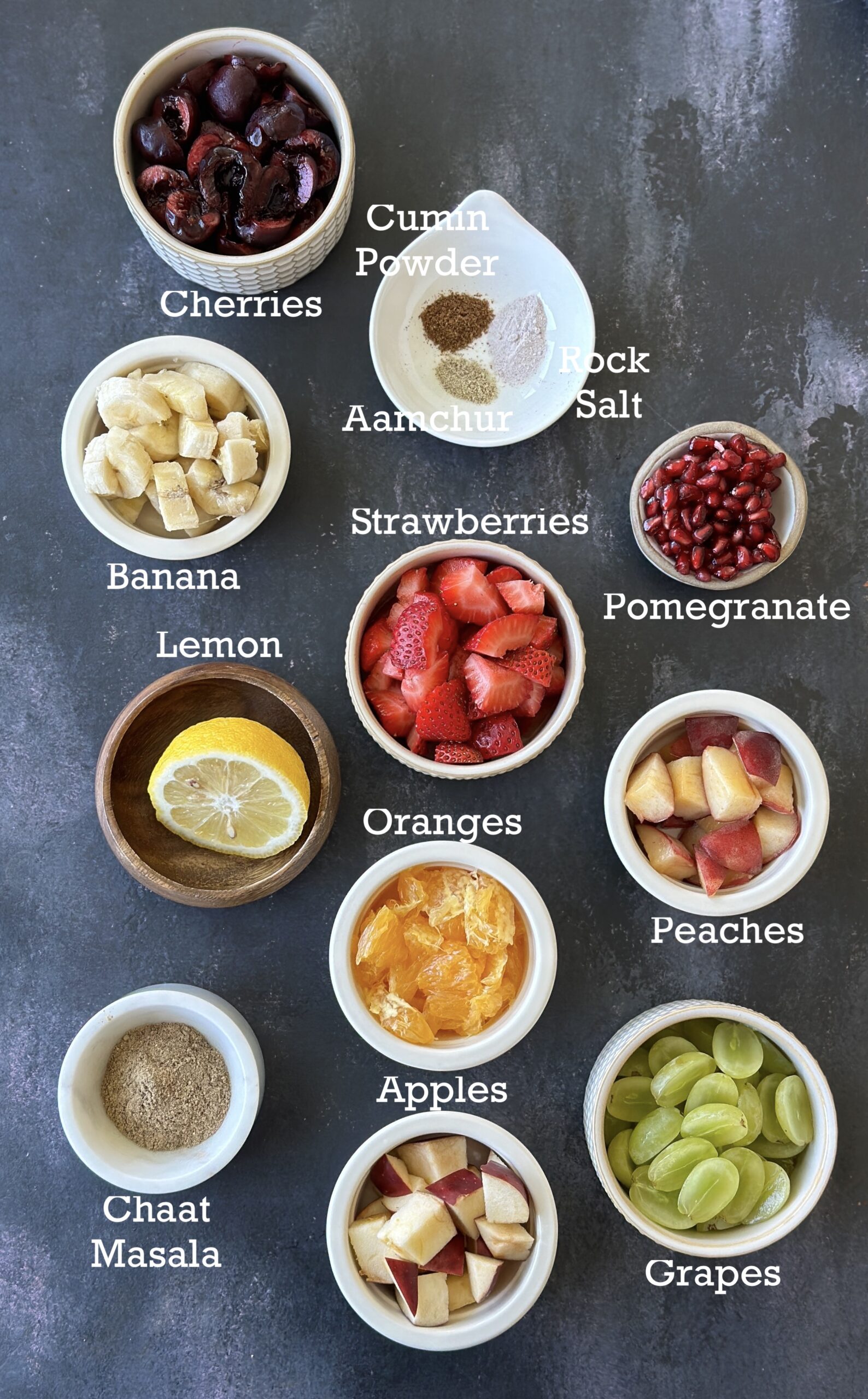 Fruit Chaat ingredients; fruits, seasonings and lemon juice on a black board. 
