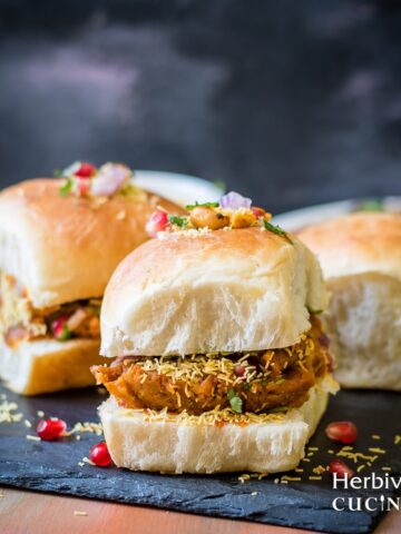 Front view of dabeli; spiced potato mix stuffed with chutneys in a pav and served on a slate platter.