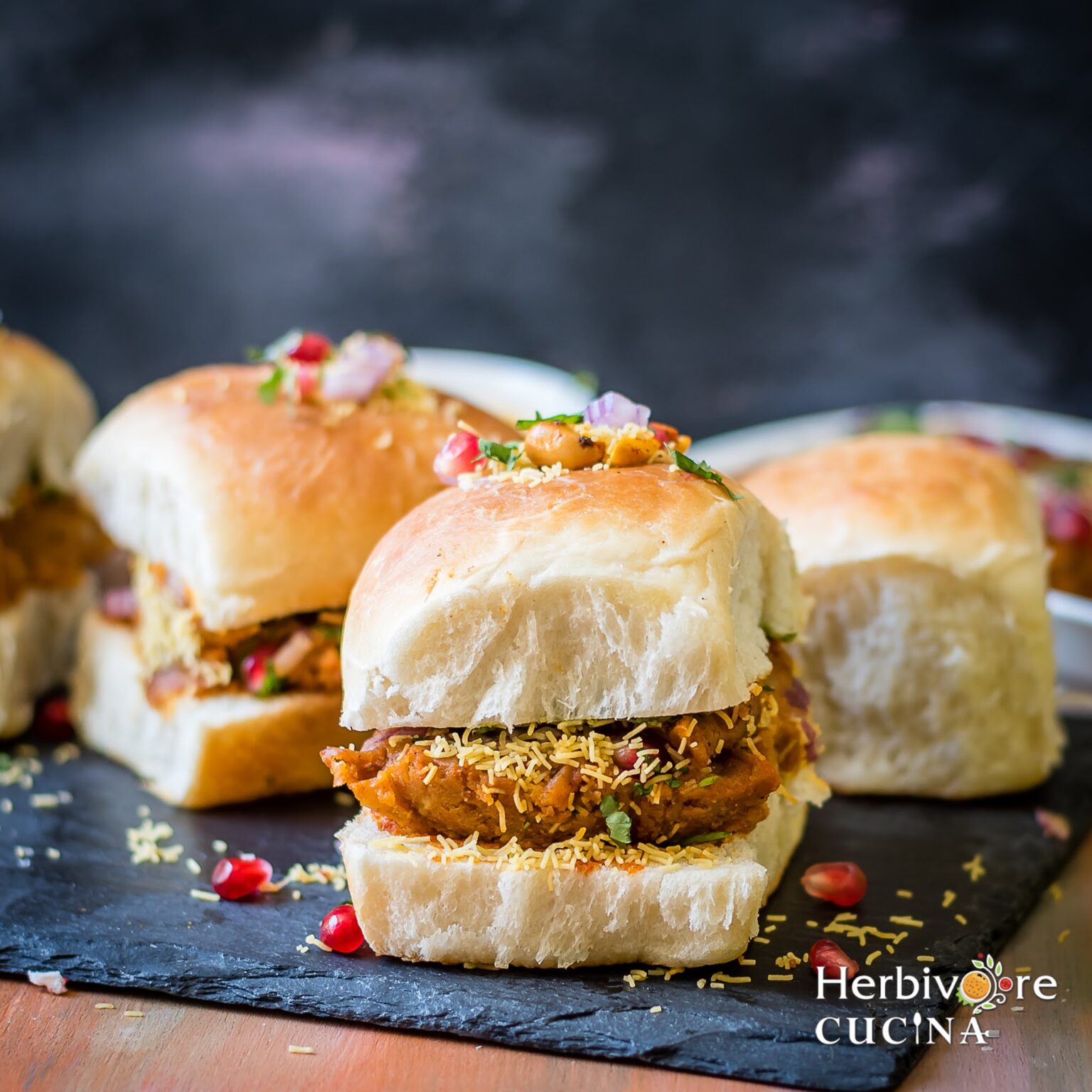 Front view of dabeli; spiced potato mix stuffed with chutneys in a pav and served on a slate platter.