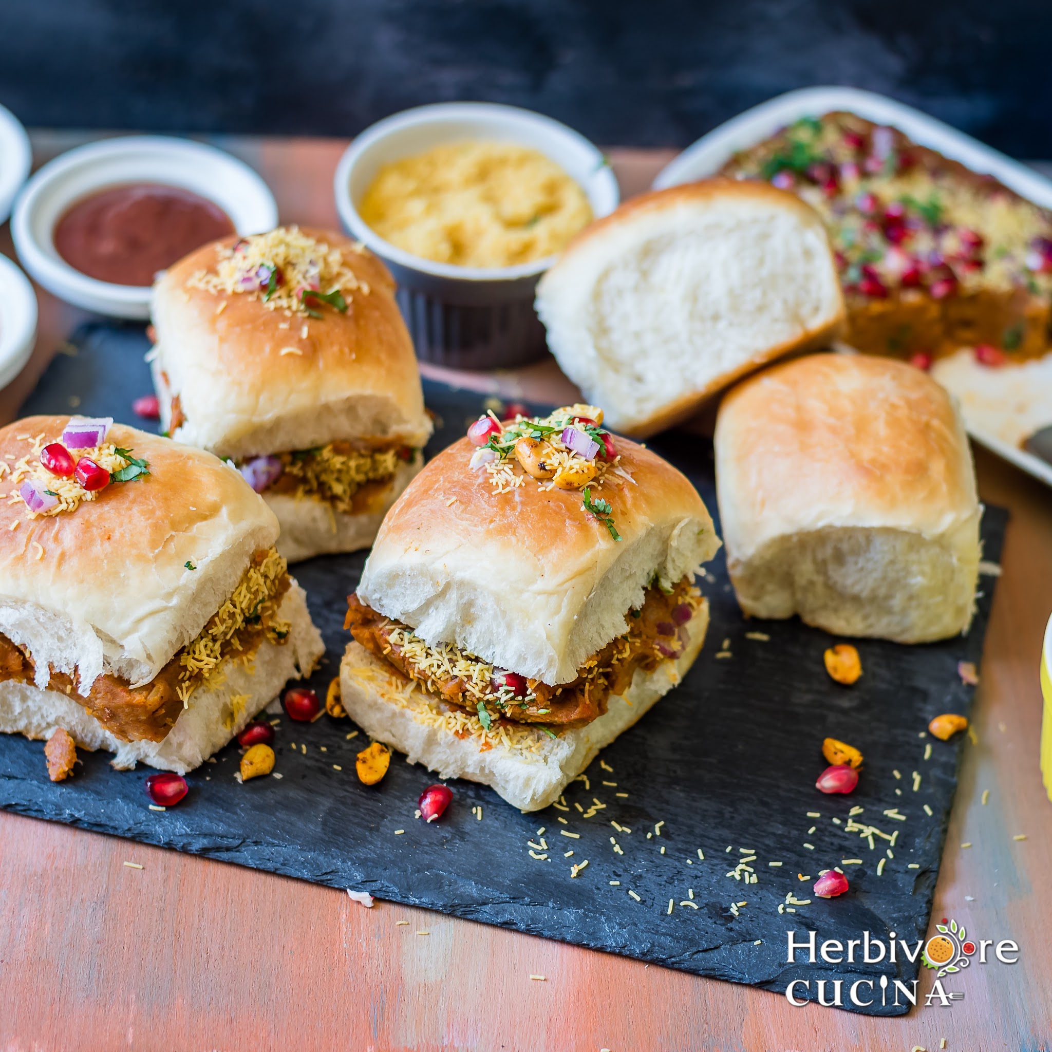 Side view of Kutchi Dabeli on a slate platter with more pav and masala on the side. 