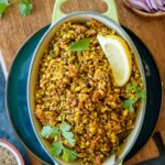 An oval platter with sprouted matki ki sabzi; topped with lemon slice and cilantro served with chopped onions on the side.