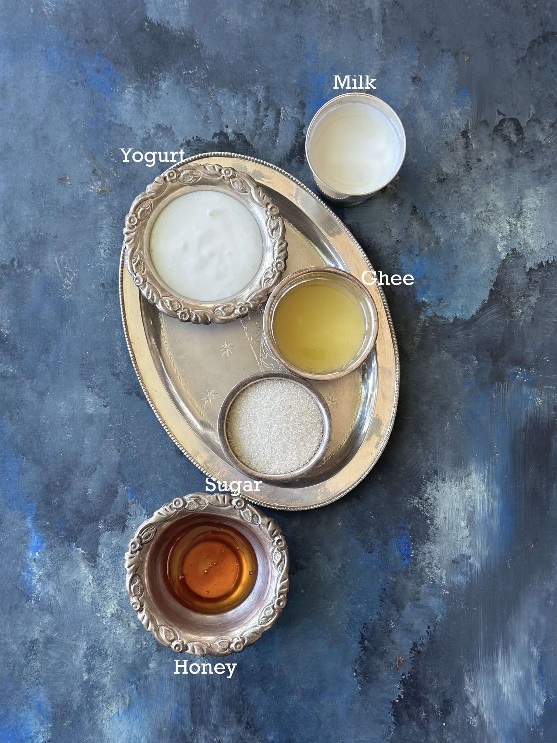 Ingredients for Panchamrit; five elements in silver bowls on a blue surface. 