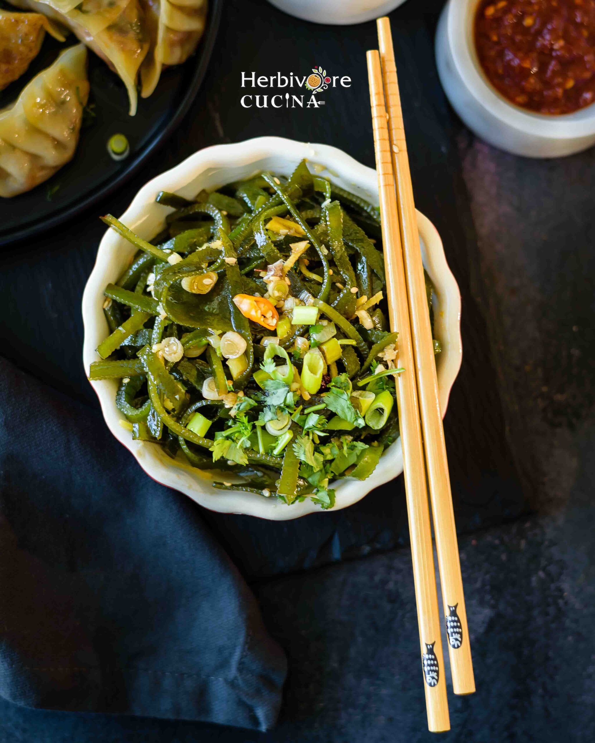 A white bowl with seaweed salad, topped with garlic and chili and a pair of chopsticks on he side. 