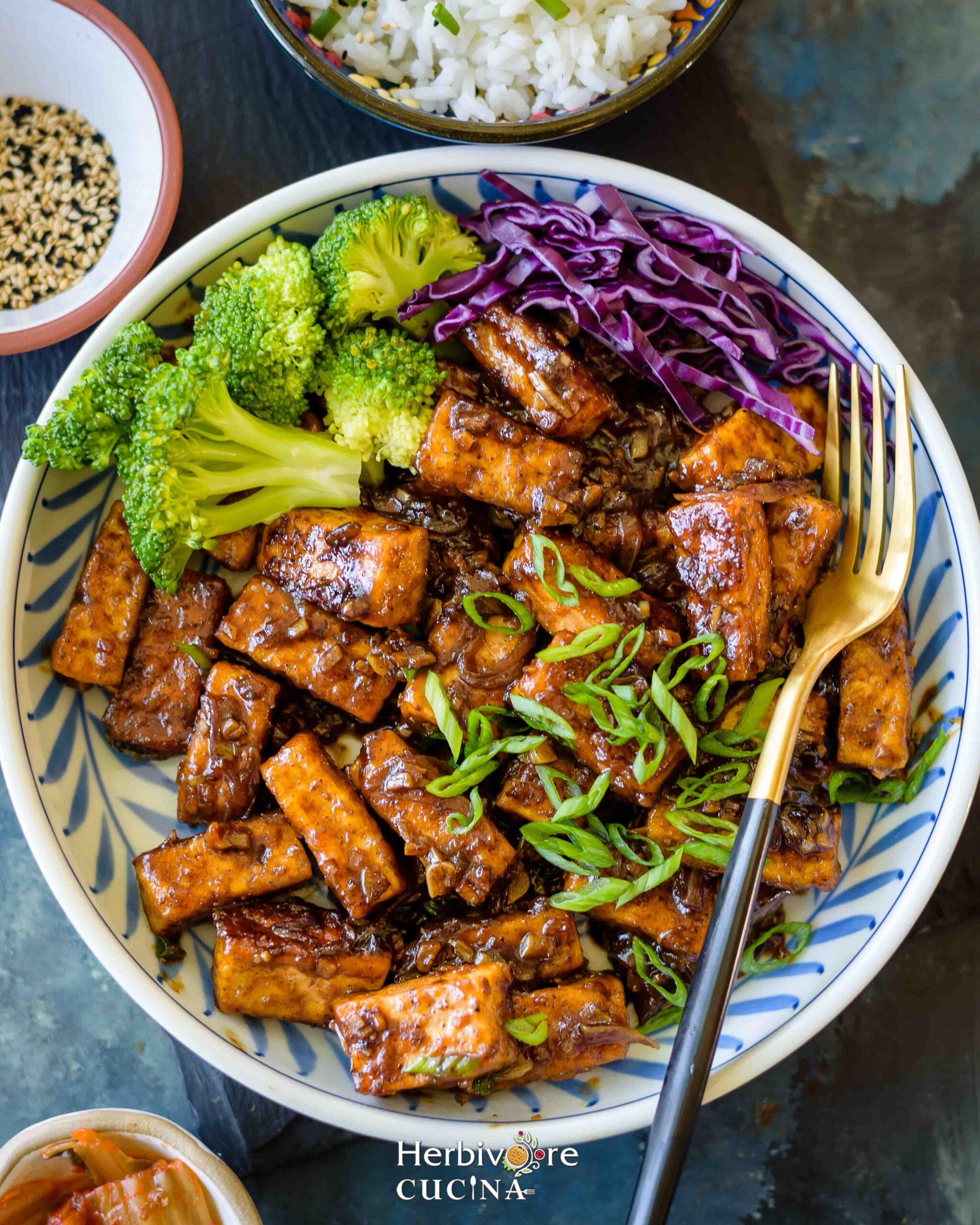 Stir fried tofu topped with scallions served with steamed broccoli and slaw in a plate. 