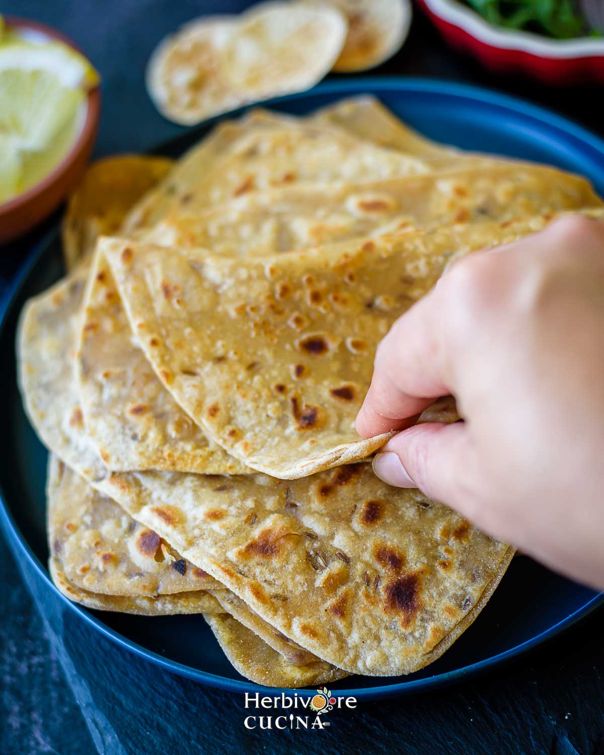 Folded triangle paratha in a blue plate with a hand breaking it into half.