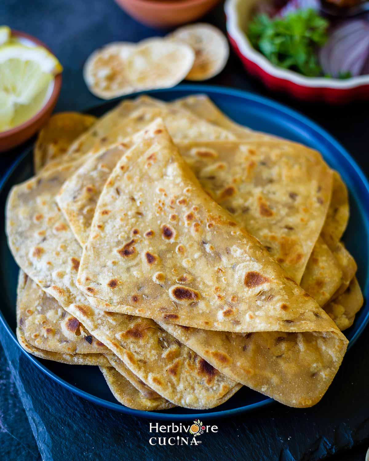 A blue plate with a stack of triangle parathas and some sides around it. 