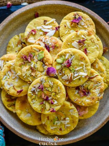 A plate with a stack of badam puris topped with nuts, saffron and dried rose petals.