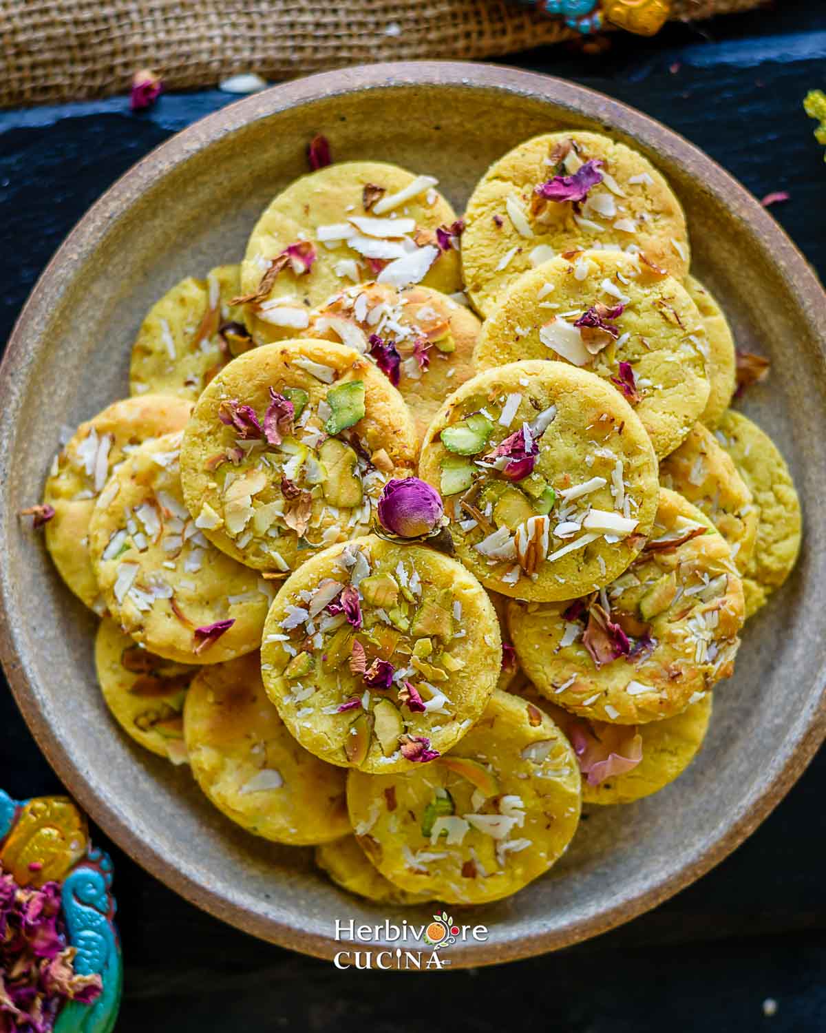 A plate with a stack of badam puris topped with nuts, saffron and dried rose petals. 