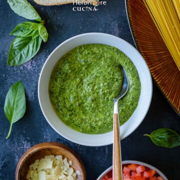 A bowl of basil pesto surrounded with other Italian ingredients.