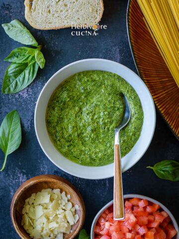 A bowl of basil pesto surrounded with other Italian ingredients.