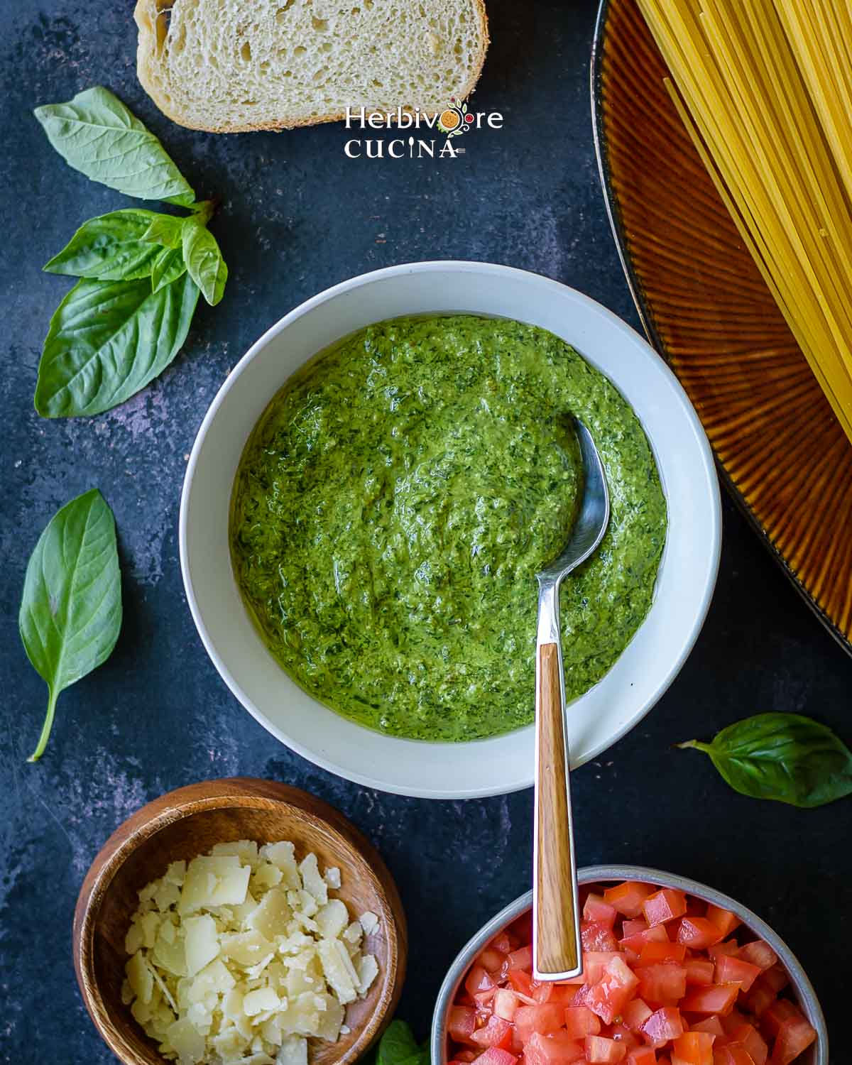 A bowl of basil pesto surrounded with other Italian ingredients. 