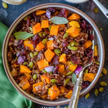 A bowl filled with butternut squash and red rice pilaf, topped with butternut squash, cranberries and pepitas.