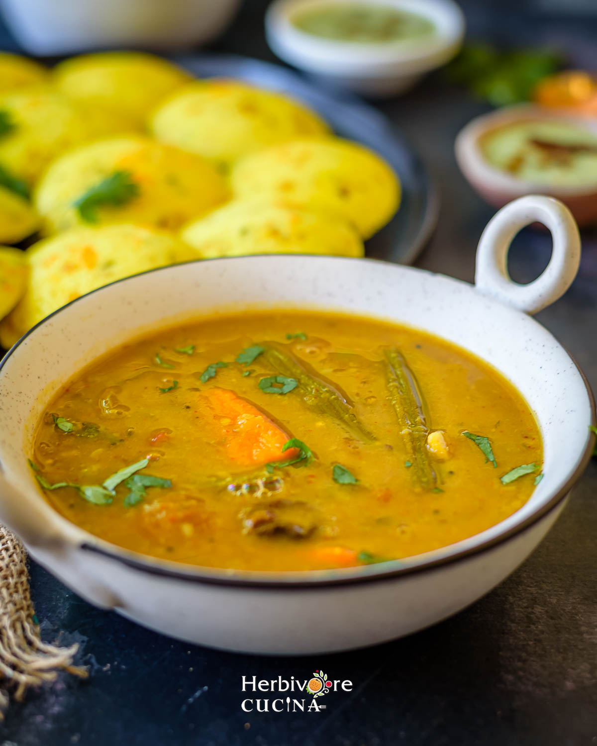 A bowl filled with sambar topped with tempering and served with idli on the side. 