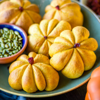 Pumpkin shaped rolls in a bowl with a small bowl with pepitas next to it.