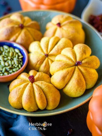 Pumpkin shaped rolls in a bowl with a small bowl with pepitas next to it.