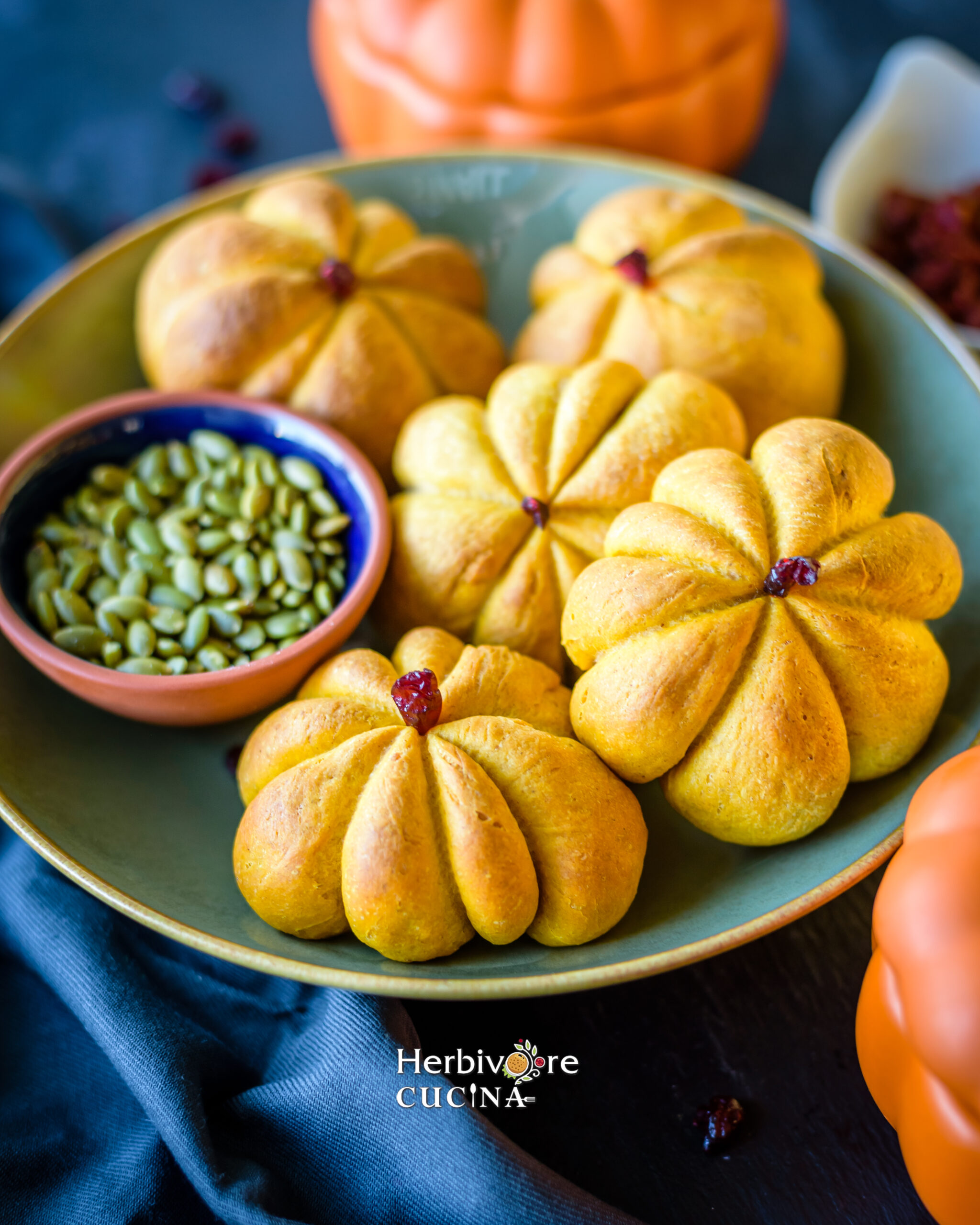 Pumpkin shaped rolls in a bowl with a small bowl with pepitas next to it. 