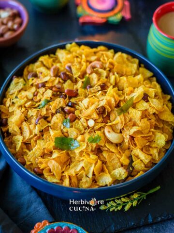 Corn Flakes Chivda in a bowl, topped with peanuts, curry leaves and dalia with chai on the side.