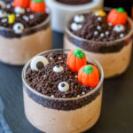 A glass container with chocolate mousse topped with oreo and halloween sprinkles.