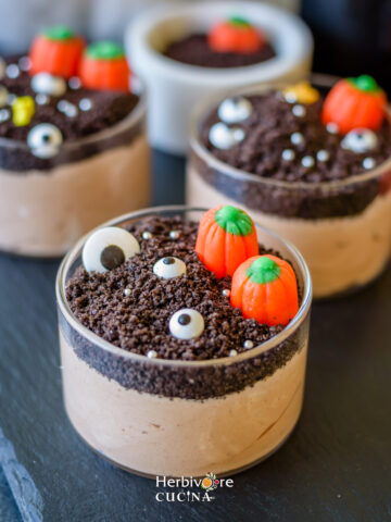 A glass container with chocolate mousse topped with oreo and halloween sprinkles.