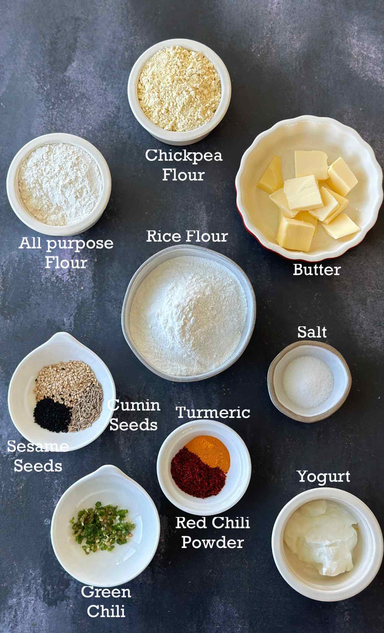 Ingredients to make rice flour chakli in small bowls on a dark surface. 