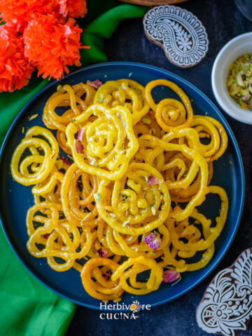 A blue plate with instant jalebi topped with pistachios and rose.
