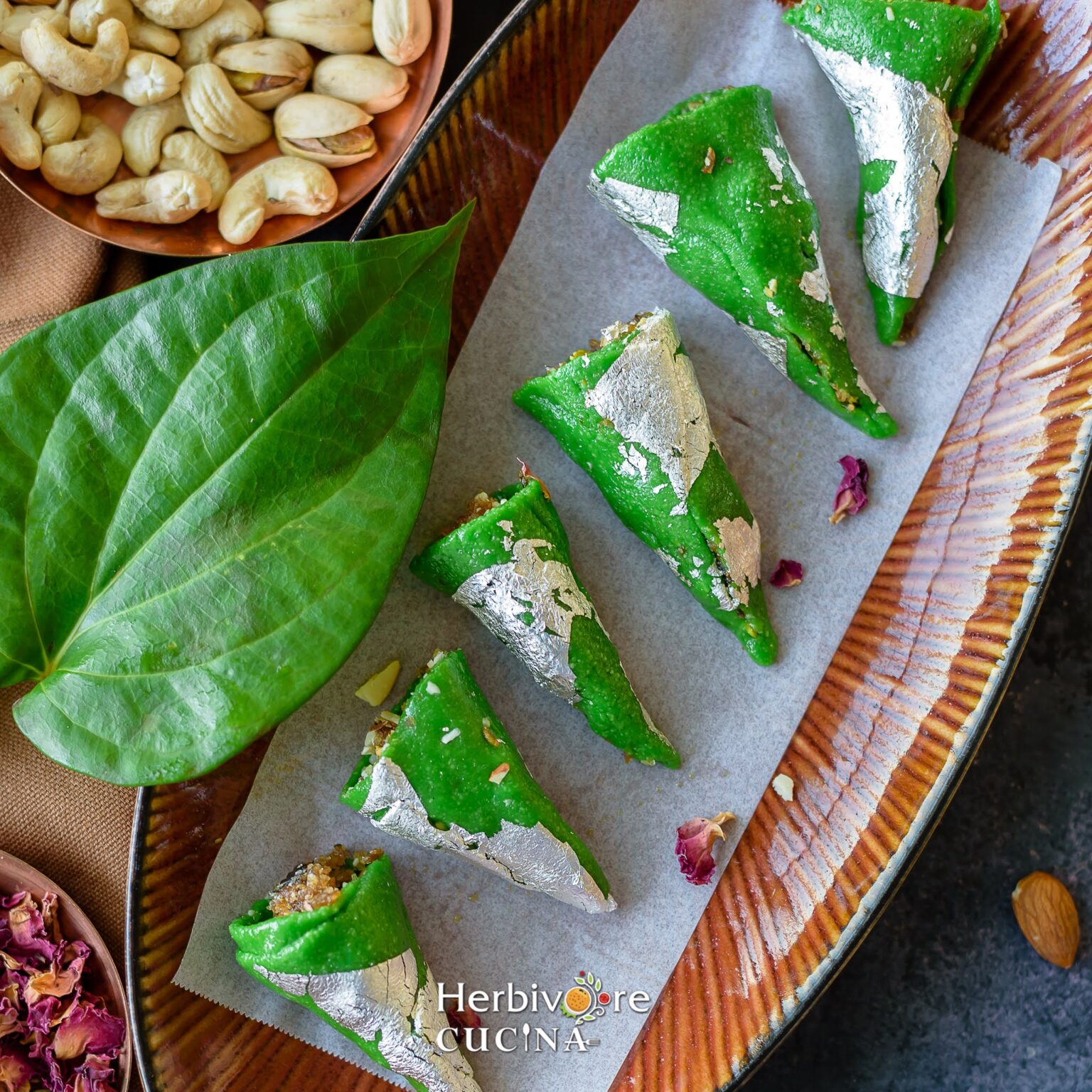 A large oval tray with kaju paan and leaves and nuts on the side. 