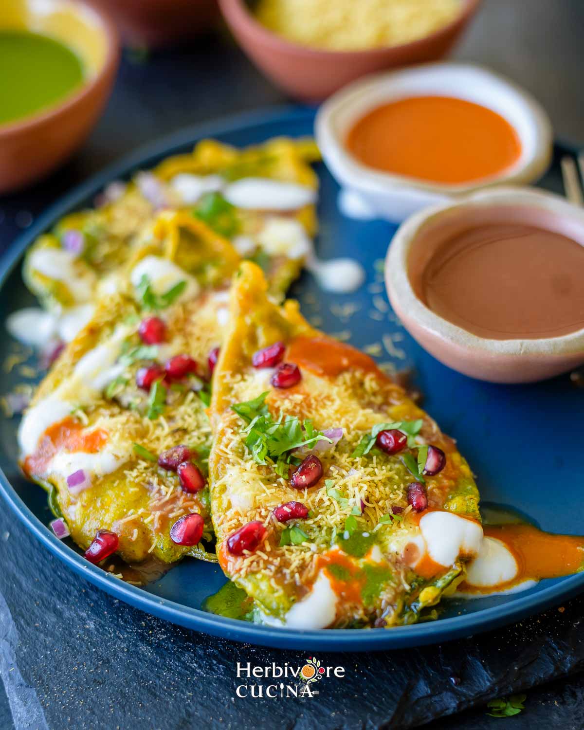 Placing fried paan leaves on a plate and topping the chaat with chutneys and toppings. 