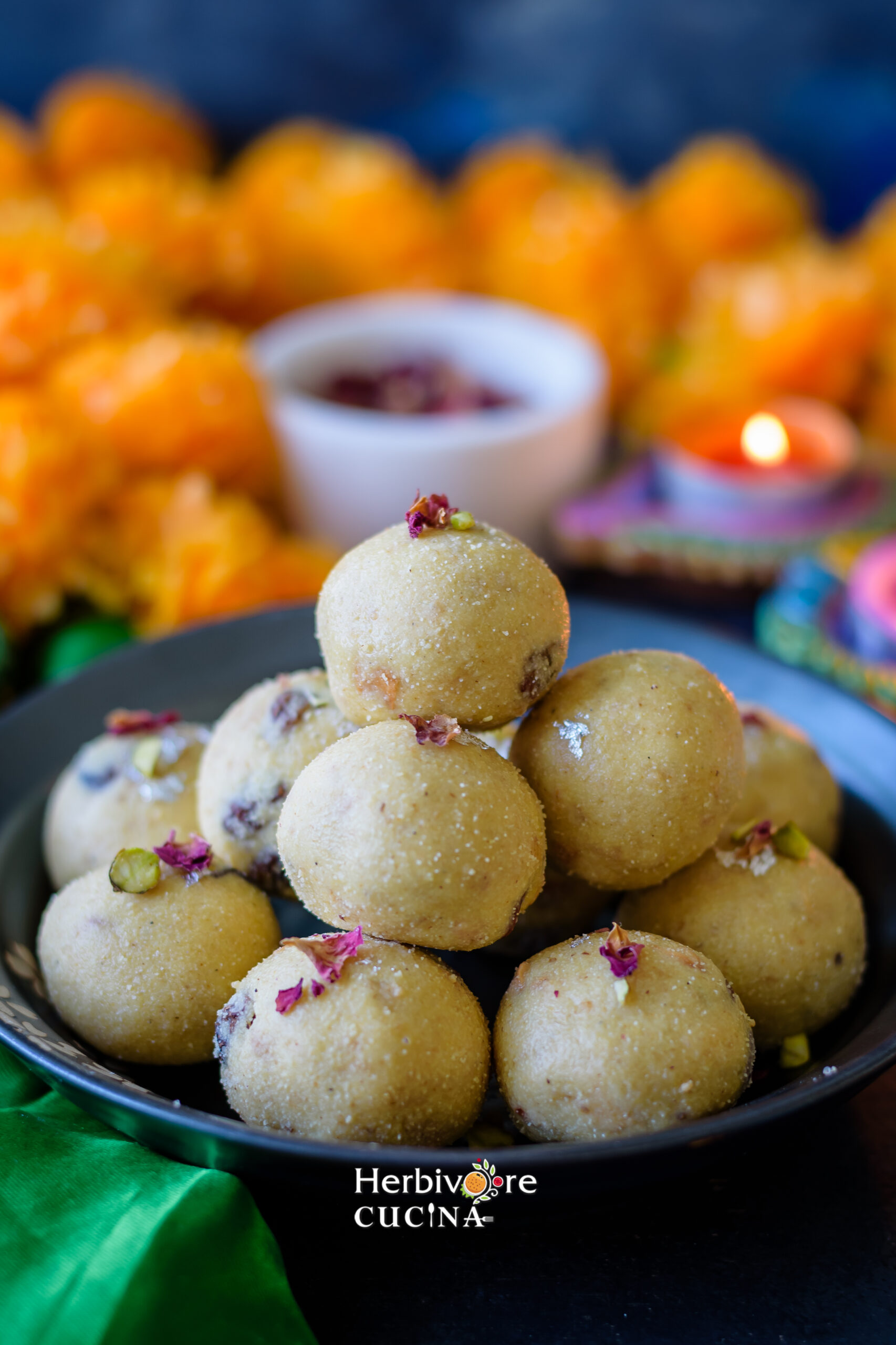 A pile of rava ladoo on a plate with rose petals and flowers in the background. 