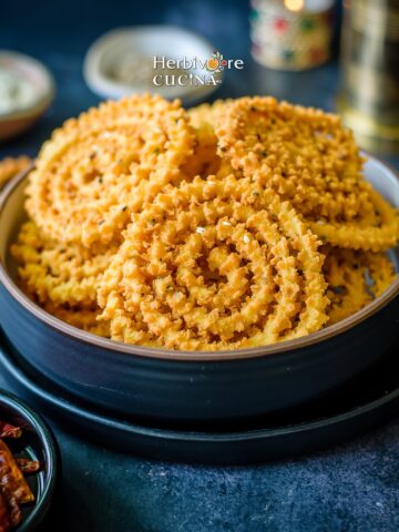 A bowl filled with rice flour chakli spirals with spices on the side.