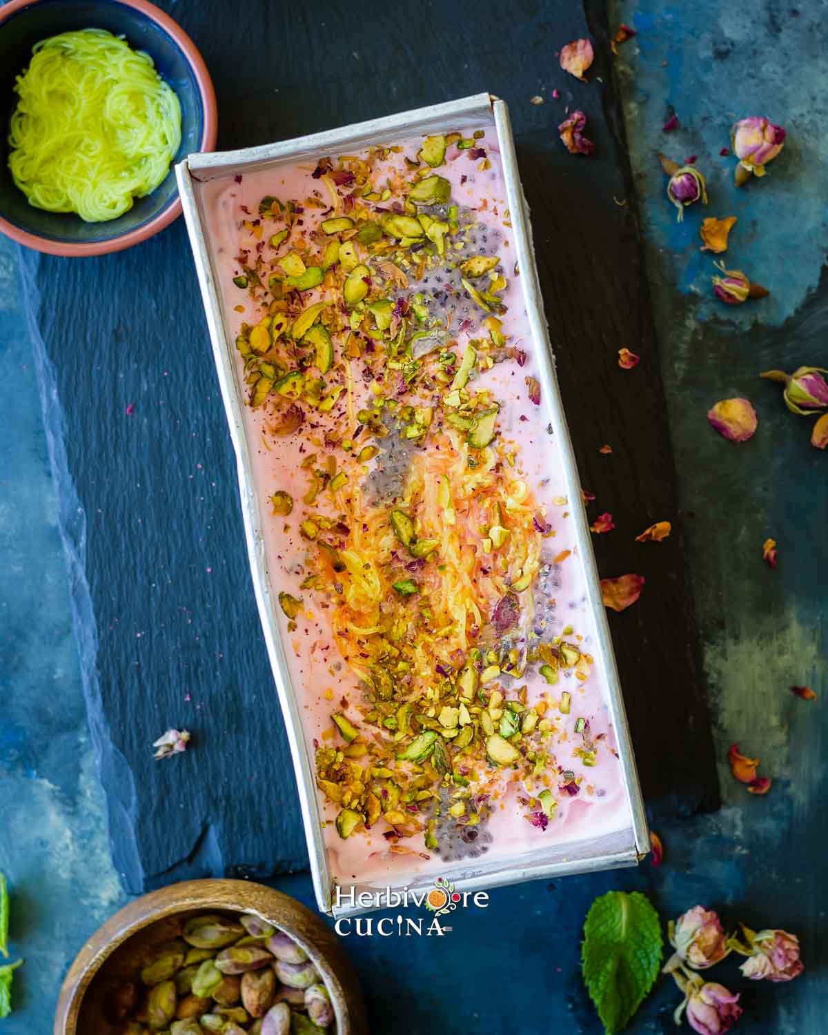 A rectangle pan with rose falooda ice cream; topped with rose syrup, takmaria and sev with nuts. 