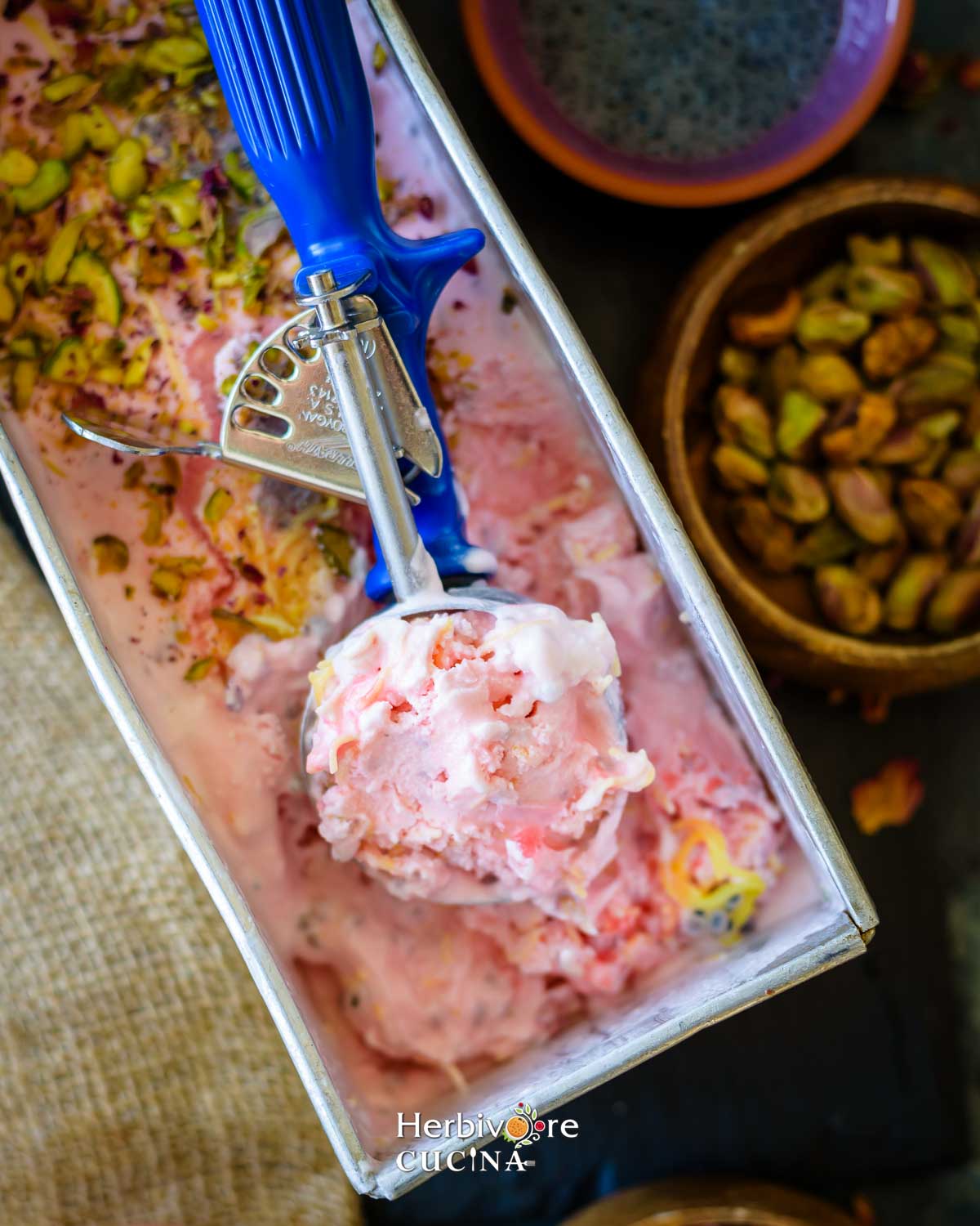 A scoop with falooda ice cream in a tray of ice cream with nuts and falooda sev. 