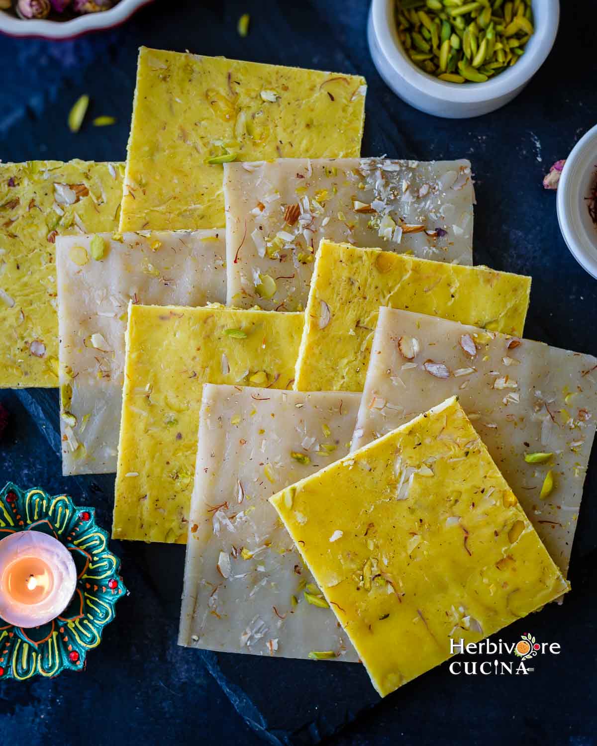 Ice Halva sheets placed on top of one another with diya and pistachios in the background. 
