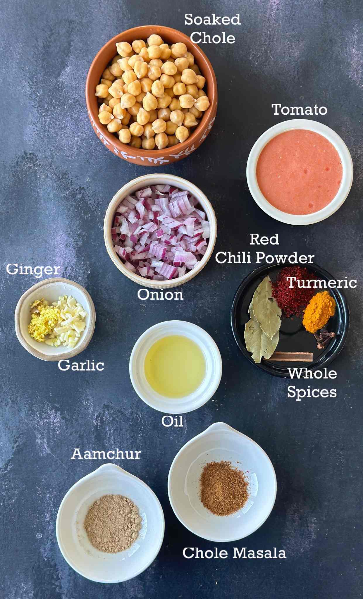 Ingredients of instant pot chole in small bowls arranged on a dark surface. 