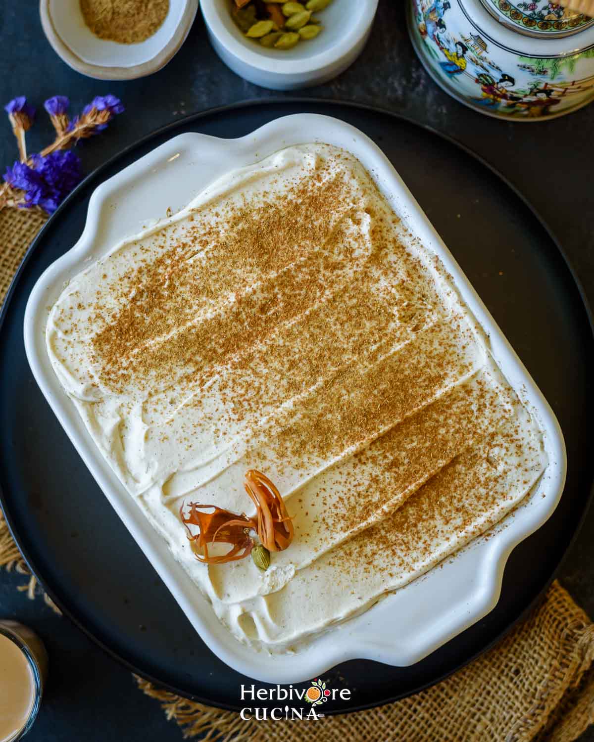 A tray filled with masala chai tiramisu topped with chai masala and served with some spices on the side. 