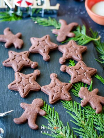 A slate with cut out cookies made with eggless chocolate dough with green leaves around it.