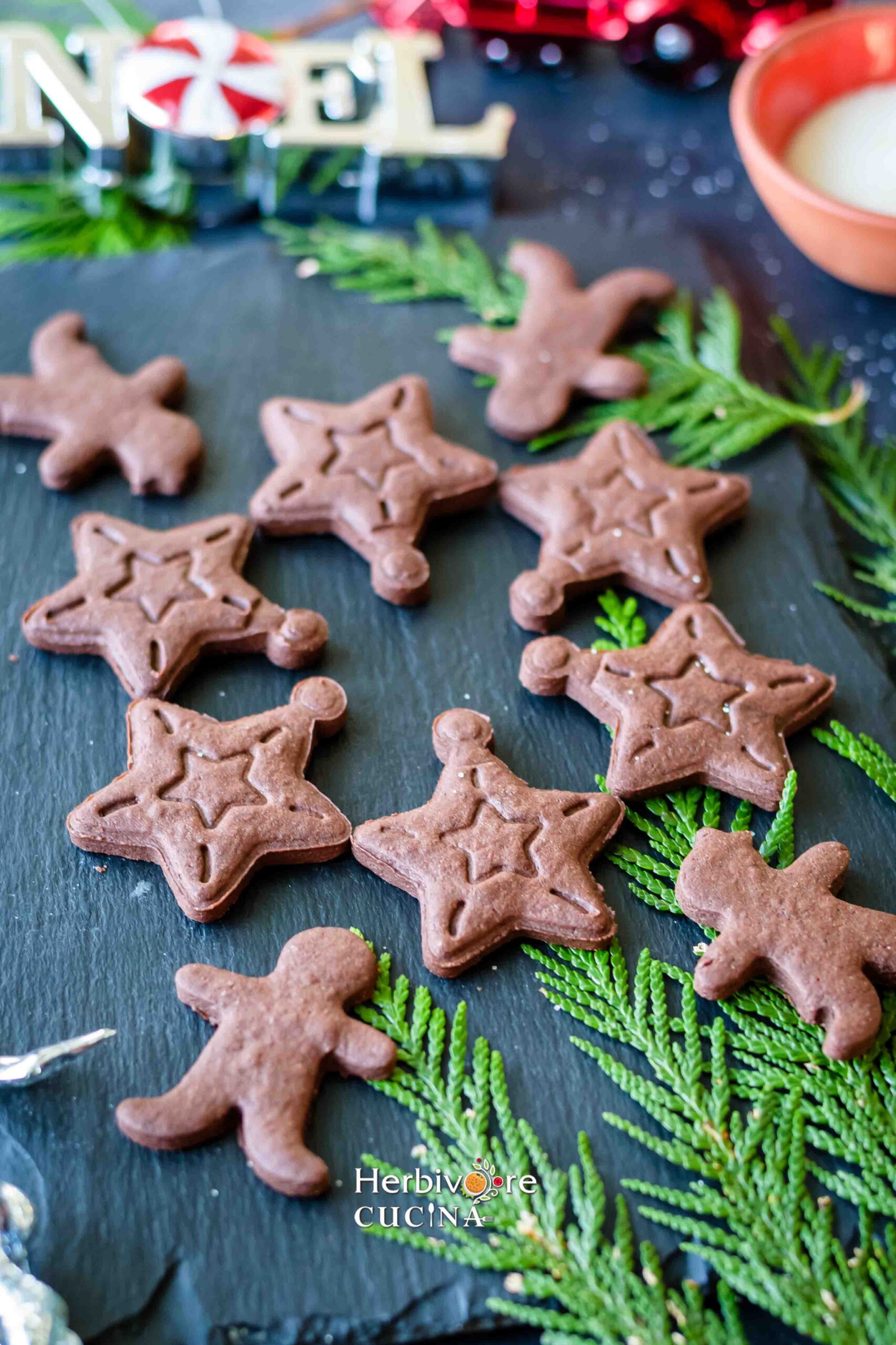 A slate with cut out cookies made with eggless chocolate dough with green leaves around it. 