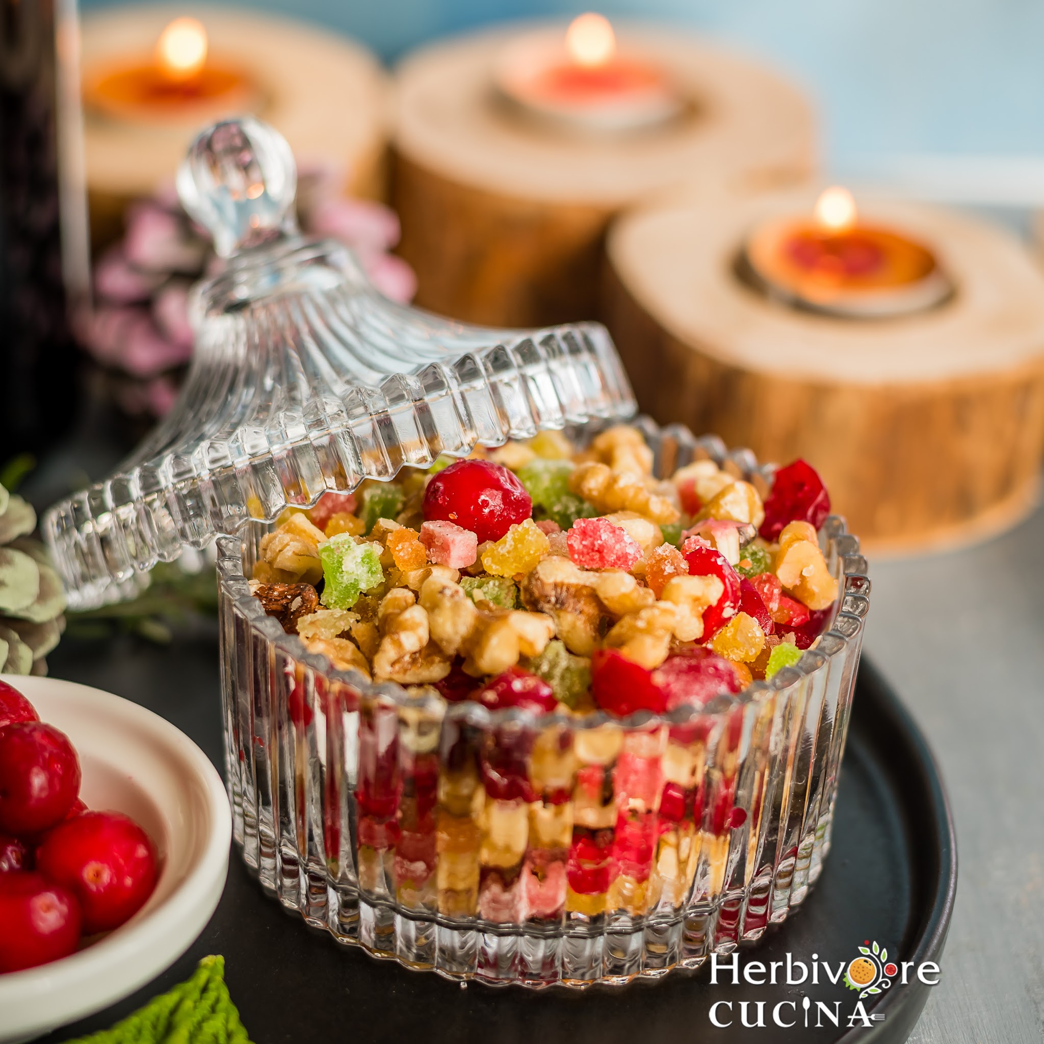 Soaked fruits and nuts in a glass jar with candles behind it. 