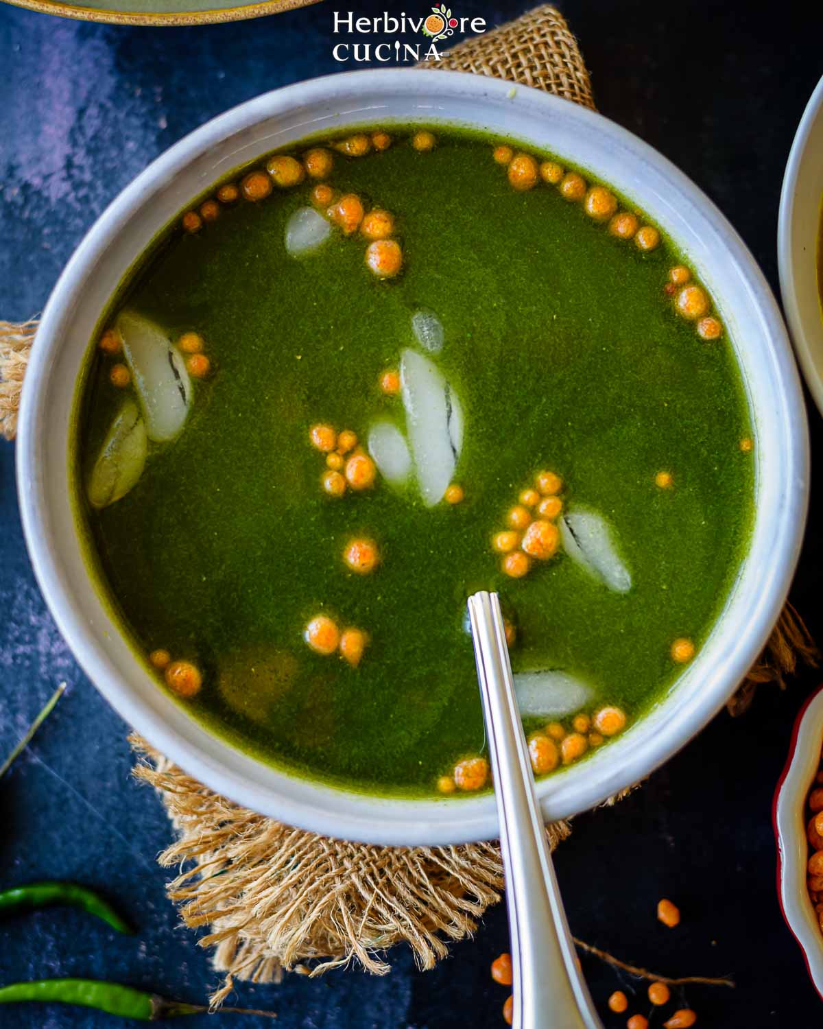 A bowl of spicy green pani for pani puri topped with boondi and ice. 