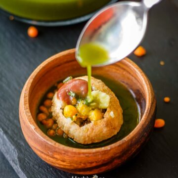 A small bowl with a prepared pani puri with a spoon dropping pani in it.