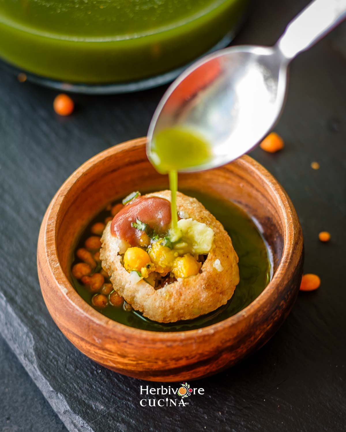 A small bowl with a prepared pani puri with a spoon dropping pani in it. 