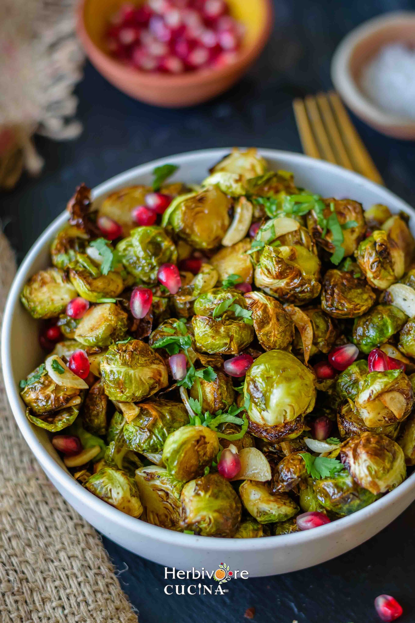 A bowl of air fryer Brussels Sprouts topped with pomegranate arils and served with cilantro leaves. 