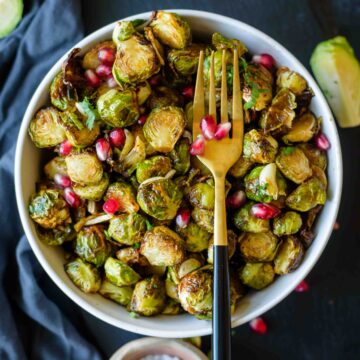 Air Fryer Brussels Sprouts in a bowl topped with pomegranate arils and a small bowl of salt beside it.
