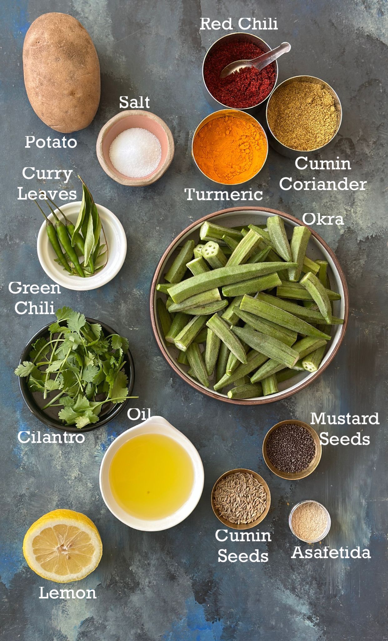 Ingredients to make bhinda bateta sabzi in small bowls on a dark background. 