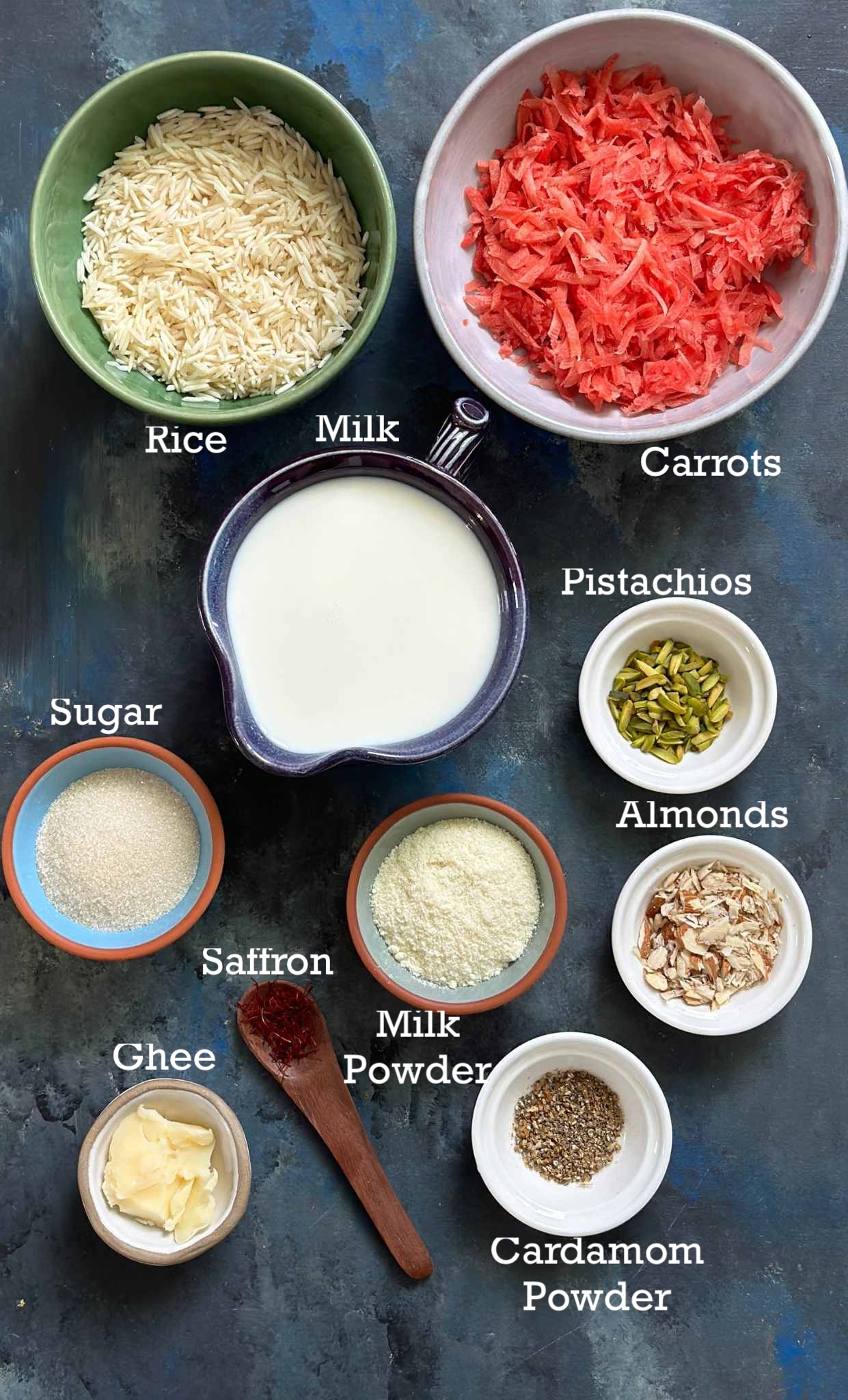 Ingredients for carrot kheer in small bowls on a dark surface. 